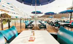 Bild av en utomhusrestaurang med bord och blå parasoller. (AI-genererad text)