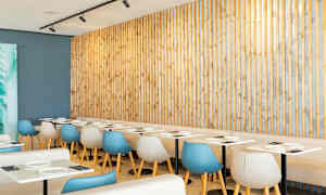 Restaurang med ljusa bord och moderna stolar framför en träpanel. (AI-genererad text)