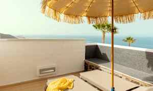 En solstol på en terrass med utsikt över havet, solparasoll och palmer. (AI-genererad text)