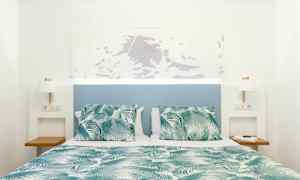 Säng med grön- och vitmönstrat täcke och kuddar, med blå sänggavel och vita väggar. (AI-genererad text)