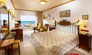 Ett hotellrum med en dubbelsäng, sittgrupp, och en balkong med utsikt mot havet. (AI-genererad text)