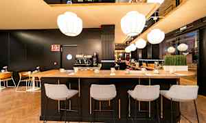 Interiör av en modern café- eller baravdelning med högbord och stolar, kaffemaskin och belysning. (AI-genererad text)