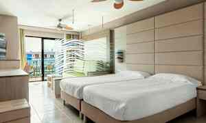 Ett hotellrum med två enkelsängar, en sittgrupp och en balkong med utsikt. (AI-genererad text)