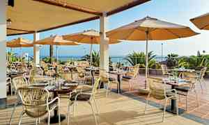 Restaurang med uteservering, bord och stolar under parasoller med utsikt över havet. (AI-genererad text)