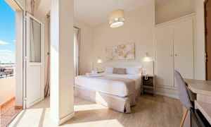 Ett hotellrum med en dubbelsäng, sängbord, skrivbord och garderob, samt en balkong med utsikt. (AI-genererad text)