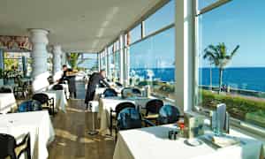 Restaurang med dukade bord nära fönster med havsutsikt. (AI-genererad text)