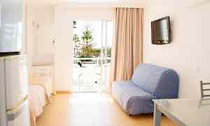 Ett ljust rum med soffa, bord och en balkong med utsikt över träd. (AI-genererad text)