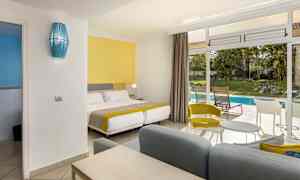 Ett hotellrum med färgglad inredning och utsikt mot en trädgård med pool. (AI-genererad text)