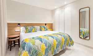 Ett modernt hotellrum med en säng klädd i färgglatt överkast och kuddar samt en spegel på väggen. (AI-genererad text)