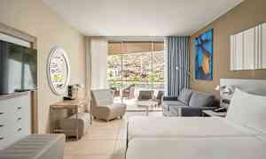 Hotelrum med två enkelsängar, soffa och sittmöbler. Glasdörrar leder till en terrass med utsikt. (AI-genererad text)