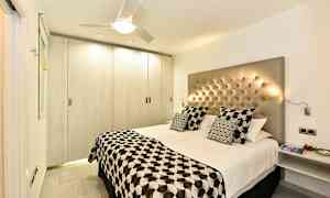 Ett modernt sovrum med en dubbelsäng, knäppad huvudgavel och mönstrade sängkläder. (AI-genererad text)