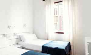 Ett hotellrum med två enkelsängar klädda i vita lakan och blå filtar. (AI-genererad text)