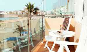 En balkong med utsikt över en strand och palmer, med bord och stolar. (AI-genererad text)