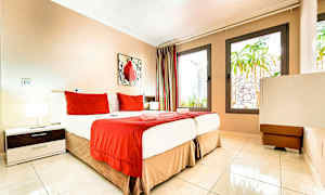 Ett hotellrum med en säng bäddad med röda och vita sängkläder samt stora fönster. (AI-genererad text)