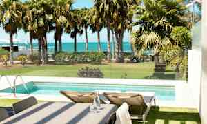 Utsikt över en pool med solstolar vid sidan, trädgård med palmer och havet i bakgrunden. (AI-genererad text)