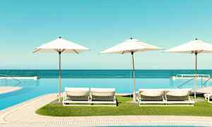 Vy av solstolar med parasoller vid en infinitypool, havet i bakgrunden. (AI-genererad text)