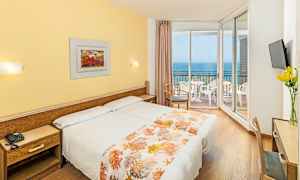 Hotellrum med två sängar, gult dekor och en balkong med utsikt över havet. (AI-genererad text)