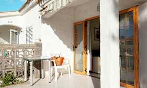 Terrass med vit byggnad, bord och stol, samt en dörr som leder in till huset. (AI-genererad text)