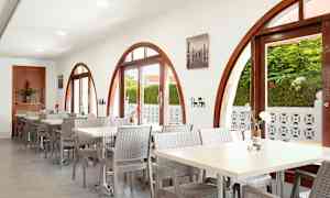 Restaurang med fönster med bågform och bord med stolar. Växter utanför synliga genom fönstren. (AI-genererad text)