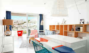 Ljust inredd lägenhet med färgglada möbler och utsikt mot ett berg genom altandörren. (AI-genererad text)