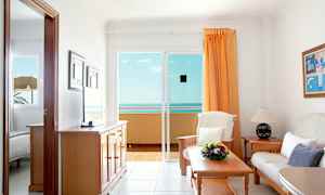 Ett vardagsrum med en soffa, bord och utsikt över havet från en glasdörr. (AI-genererad text)