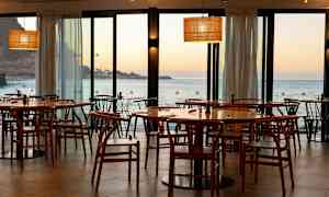 Restaurang med trästolar och bord med utsikt över havet och solnedgång. (AI-genererad text)