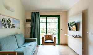 Ett vardagsrum med en blå soffa, rottingfåtölj och en TV monterad på väggen. (AI-genererad text)