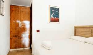 Ett litet rum med en träbädd och vita sängkläder. På väggen hänger en tavla med en måneillustration. (AI-genererad text)