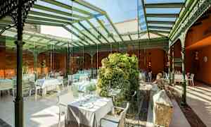 Inomhusservering med glasväggar och tak, dekorerad med grönska och bord. (AI-genererad text)