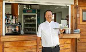 En person håller en bricka med två glas framför en serveringsdisk i trä. (AI-genererad text)