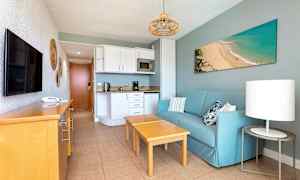 Lägenhetsrum med blå soffa, trämöbler och köksdel. (AI-genererad text)