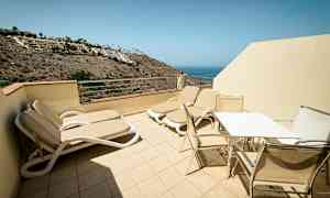 Terrass med solsängar och bord med stolar, utsikt mot havet. (AI-genererad text)