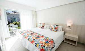 Ett hotellrum med två enkelsängar, färgglada kuddlakan och en dörr till en terrass. (AI-genererad text)