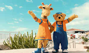 Två figurer i djurkostymer, en giraff och en björn, står bredvid varandra och vinkar, klädda i färgglada kläder. (AI-genererad text)