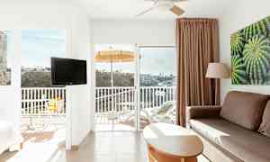 Interiör av ett ljust hotellrum med balkong, utsikt över en dal. (AI-genererad text)