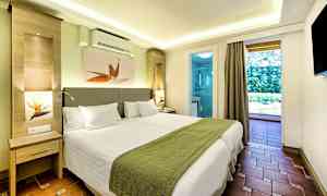 Ett modernt hotellrum med två enkelsängar, grön sängklädsel och vit inredning, med utsikt mot en balkong och badrum. (AI-genererad text)