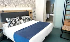 En modern hotellrum med dubbelsäng, blå överkast och två mönstrade kuddar. (AI-genererad text)