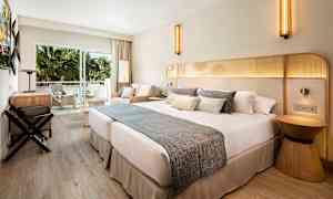 Ett hotellrum med en stor dubbelsäng, sittgrupp och balkong med utsikt mot gröna palmer. (AI-genererad text)