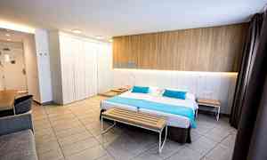 Ett modernt hotellrum med en dubbelsäng, en träbänk vid fotändan och ett skrivbord i ena hörnet. (AI-genererad text)