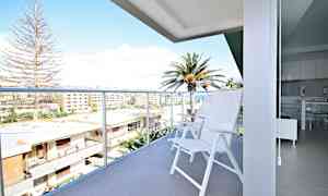 En balkong med vita stolar och utsikt över byggnader och palmer. (AI-genererad text)