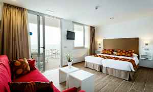 Ett modernt hotellrum med två enkelsängar, röda soffmöbler och en balkong med havsutsikt. (AI-genererad text)