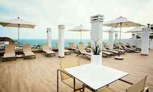 En terrass med solstolar, parasoll och utsikt över havet. (AI-genererad text)