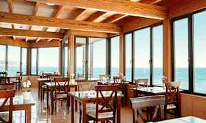 Ett café med träbord och stolar, med stora fönster som visar havsutsikt. (AI-genererad text)