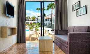 Vy av ett vardagsrum med soffa och bord samt en öppning till balkong med utsikt över en pool. (AI-genererad text)