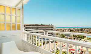 Utsikt från en balkong med sittmöbler, mot en byggnad och havet i bakgrunden. (AI-genererad text)