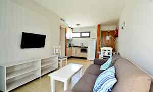 En modern hotellrumslägenhet med en soffa, TV, bord och kök. (AI-genererad text)