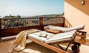 Två solstolar med randiga dynor står på en terrass med utsikt över grönskande kullar. (AI-genererad text)