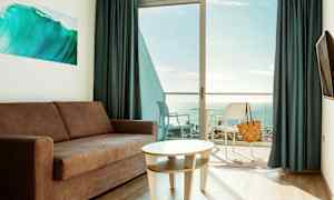 Ett vardagsrum med soffa och bord, med en balkong och utsikt över havet. (AI-genererad text)