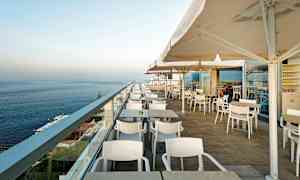 Bild av en utomhusterrass med bord, stolar och parasoller, med utsikt över havet. (AI-genererad text)