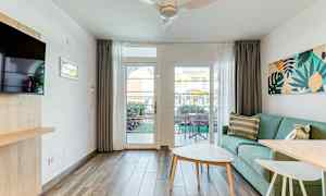 Ett ljust vardagsrum med en grön soffa, ett soffbord och en utsikt mot en terrass genom ett glasfönster. (AI-genererad text)